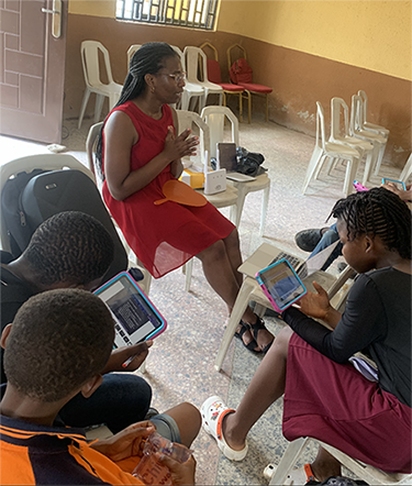 Ruth Oliwe sitting in classroom with students looking at ipads and comics worksheets